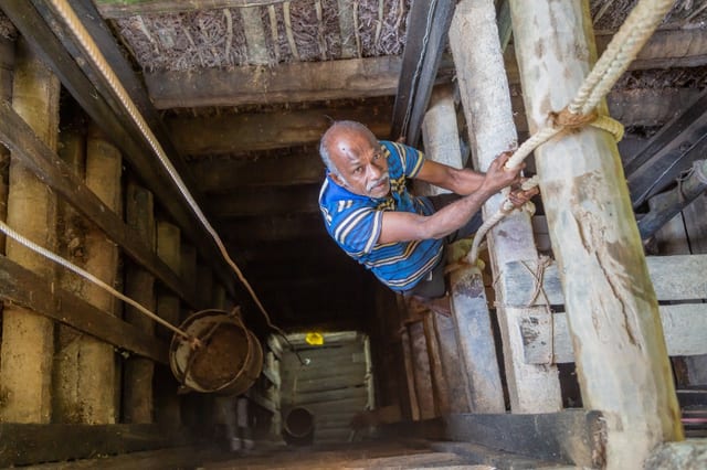 Traditional artisanal sapphire mining shaft in Sri Lanka with a miner climbing a wooden ladder