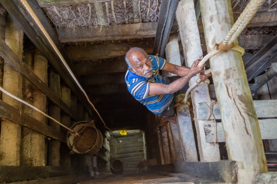 Traditional artisanal sapphire mining shaft in Sri Lanka with a miner climbing a wooden ladder